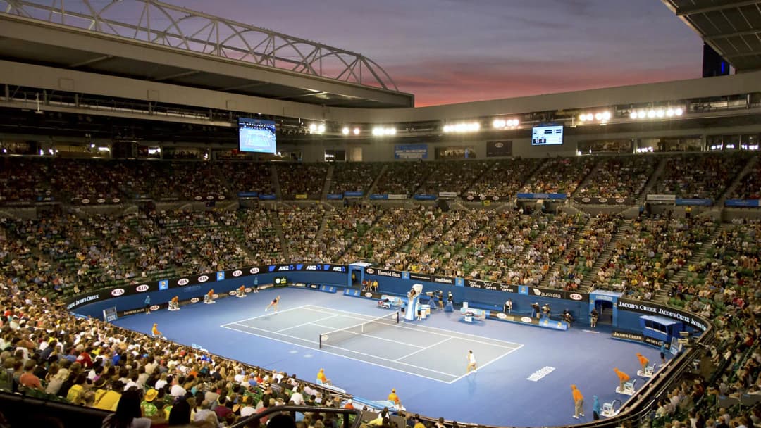 Rod Laver Arena at dusk, blue hard court packed with spectators during a match