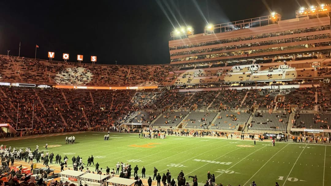 Floodlit college football stadium at night, the stands full around the field
