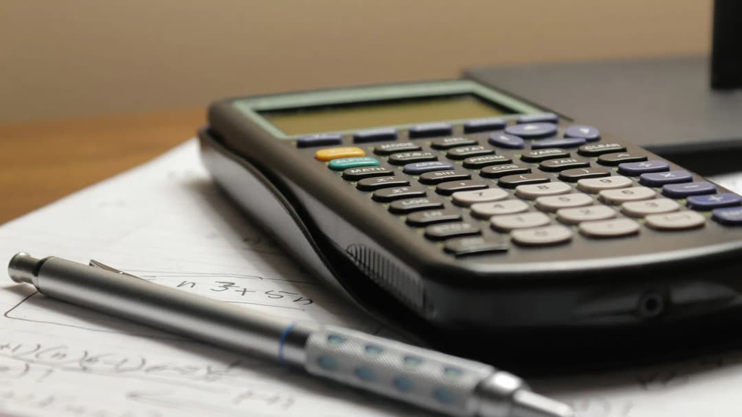 A black calculator and a pen resting on a sheet of handwritten figures.