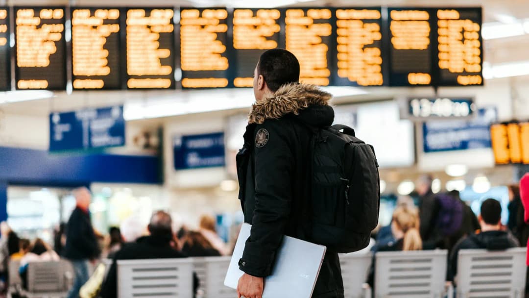 Traveler with a backpack looking up at a busy airport departures board