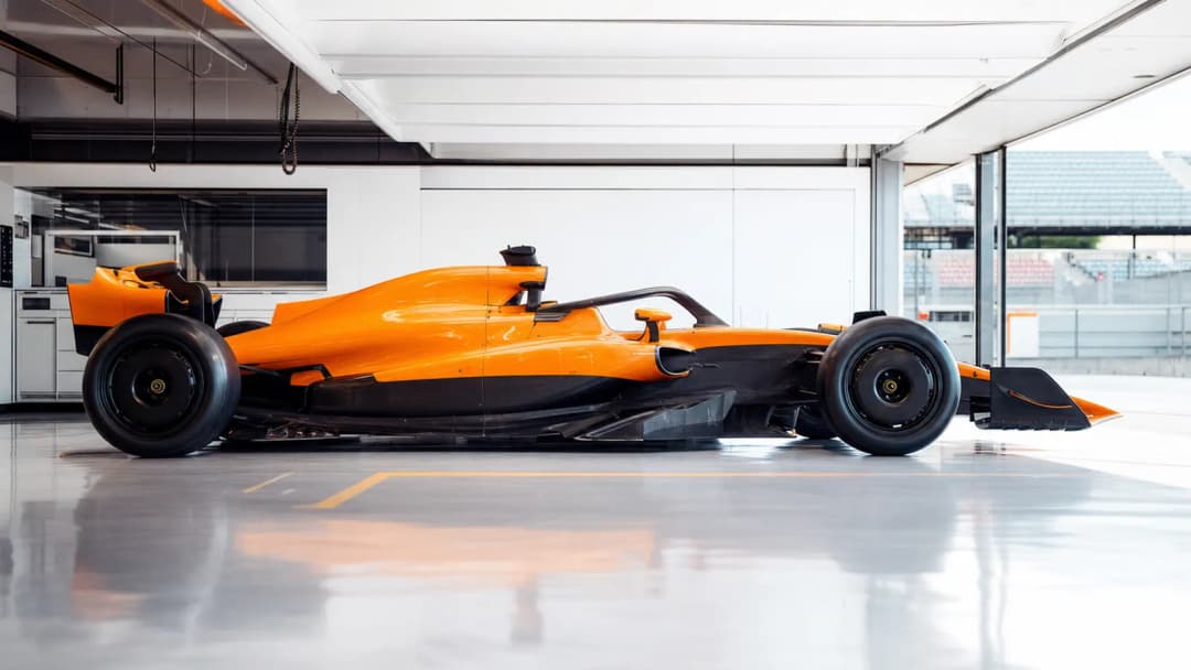 Orange Formula One race car parked in a bright team garage with soft daylight