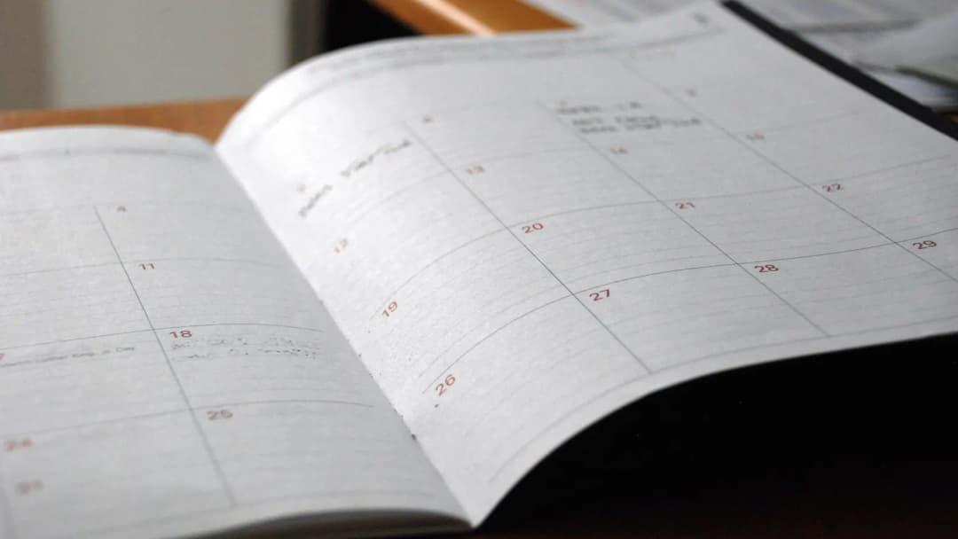 Open paper planner showing a month grid with dates on a desk