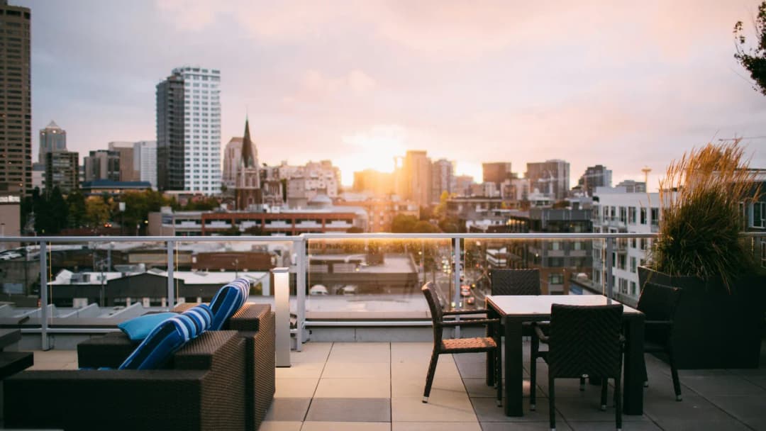 Rooftop terrace at sunset with lounge seating and a city skyline behind it.