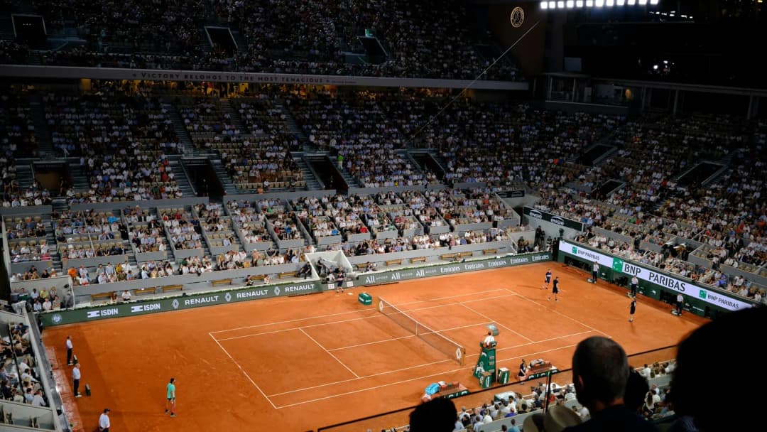Clay tennis court and packed grandstands under stadium lights during a match