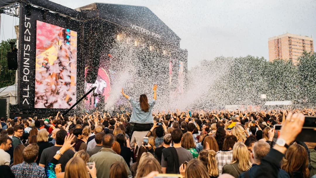 Crowd in front of the All Points East stage, with the festival name on a banner beside the screen.