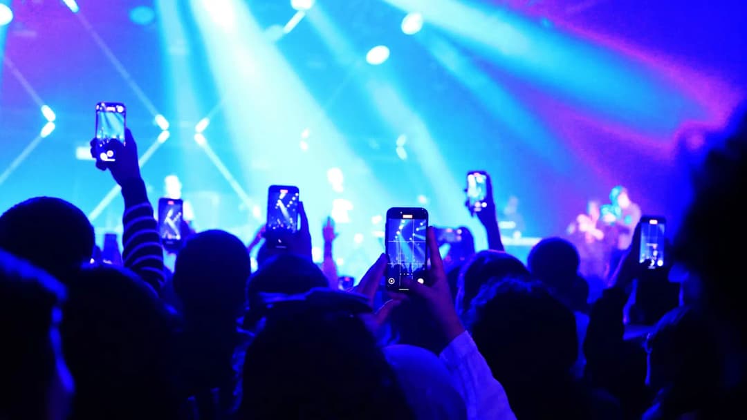 Silhouetted concert crowd with phones raised under blue and violet stage lights
