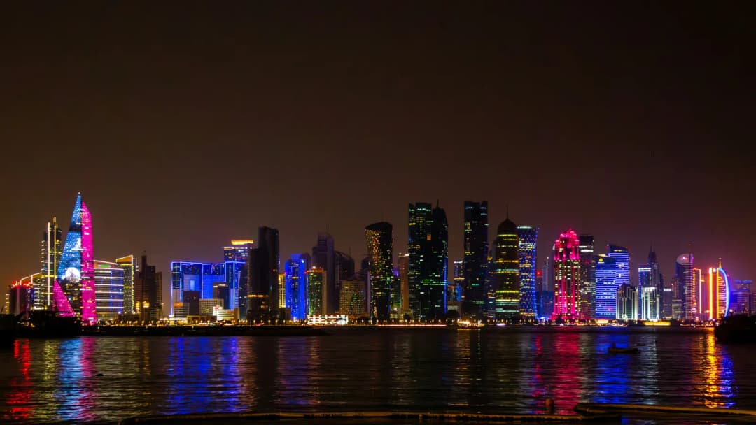 City skyline lit up at night, towers reflected in dark water