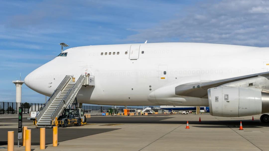White airliner parked on an apron beside a boarding staircase under a blue sky