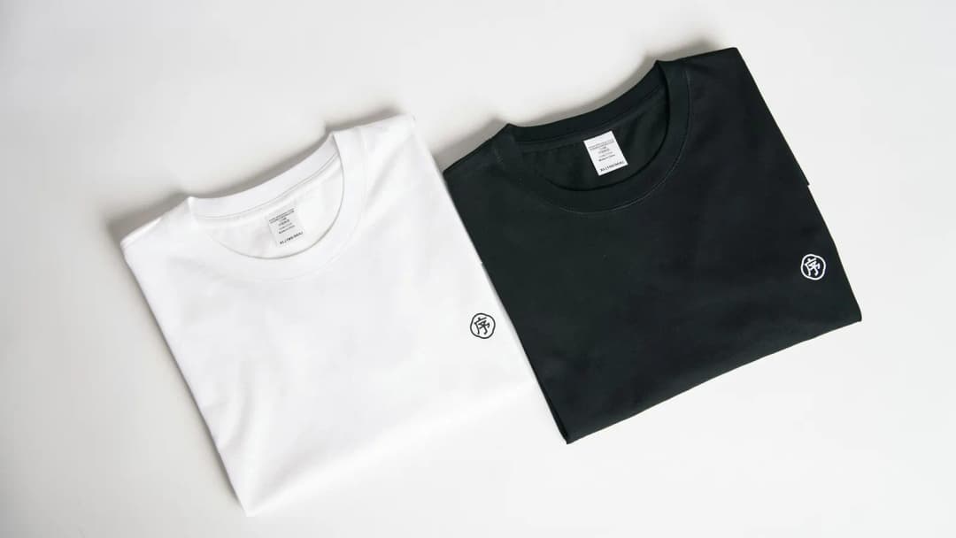 Two folded white and black crew-neck t-shirts laid flat on a plain white background