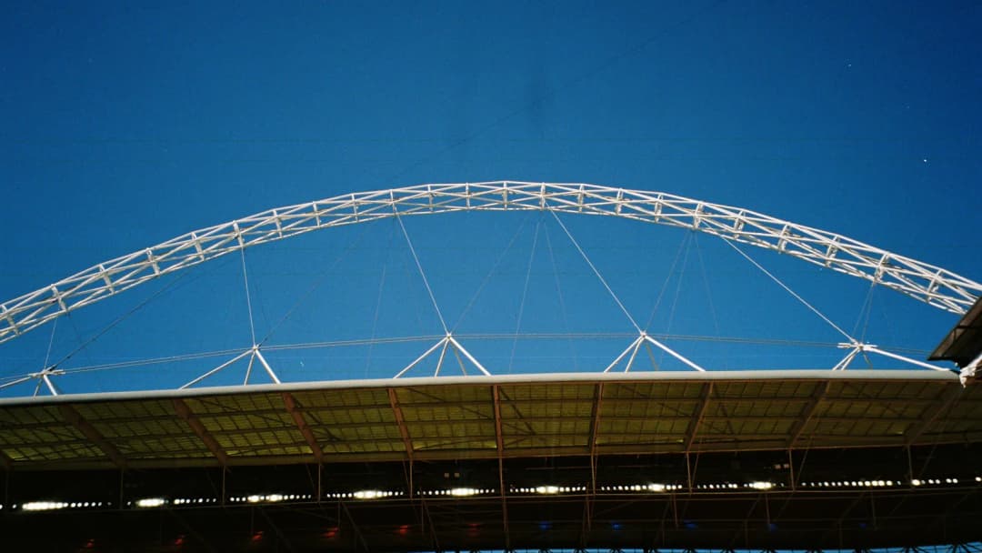 Wembley Stadium's steel arch against a clear blue sky above the stands