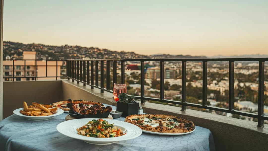 A plated dinner on a rooftop terrace, with city rooftops and hills in the distance.
