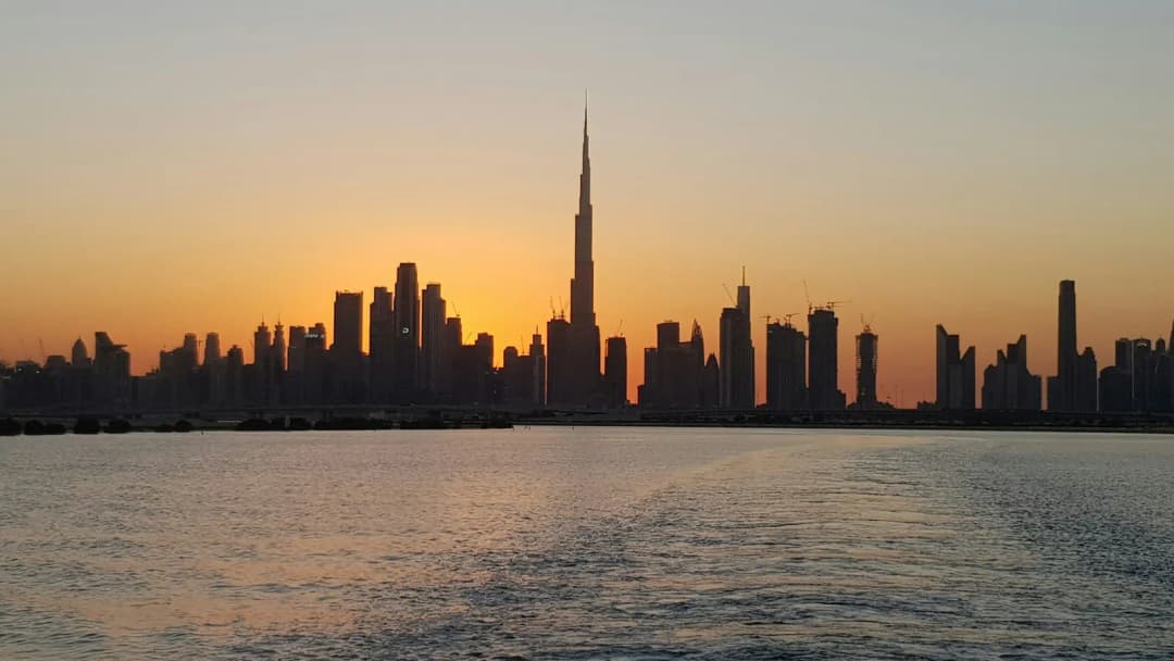Burj Khalifa and the Dubai skyline silhouetted against a golden sunset over calm water.