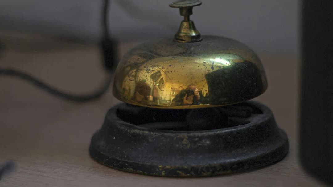 Close-up of a brass hotel desk bell on a dark, neutral surface