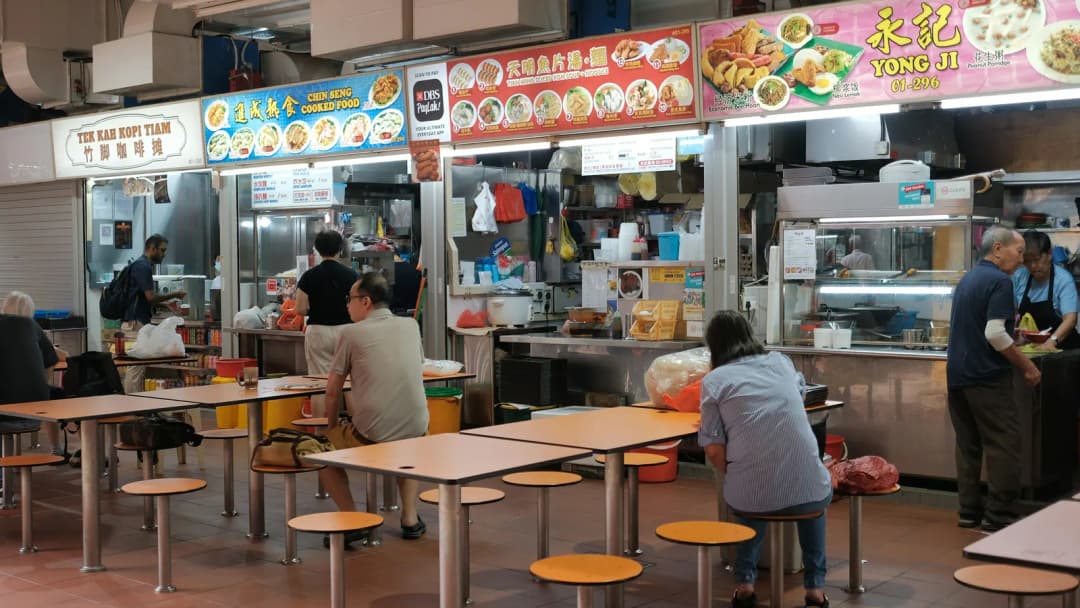 Open-air hawker centre with food stalls, bright signs and diners at tables