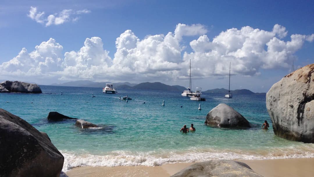 Caribbean beach with granite boulders, turquoise water and anchored boats